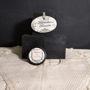 May include: Two round ceramic tags with black trim. The top tag is white with black text that reads "Fabrication Française". The bottom tag is white with black text that reads "Chateau de Vaux 1986".