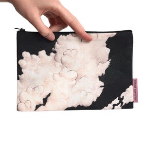 Op de afbeelding: Zwarte etui met ritssluiting en een wolkenontwerp. De etui heeft een zwarte achtergrond met een wit en beige wolkenpatroon. Een klein roze label met witte tekst is aan de zijkant bevestigd.