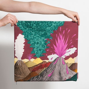 May include: A colorful fabric panel with a design of erupting volcanoes. The volcanoes are depicted in shades of gray, brown, and green, with pink and white smoke plumes. The background is a deep red color.