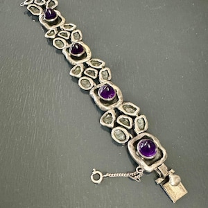 May include: A silver bracelet with a chain clasp and four purple gemstones set in silver.