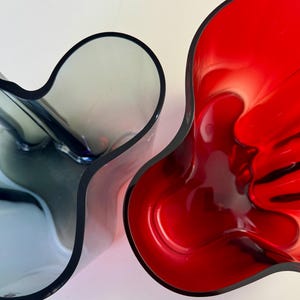 Könnte beinhalten: Zwei Vasen, eine rote und eine blaue, mit einem einzigartigen, organischen, wellenförmigen Design. Die Vasen sind aus Glas und haben eine glänzende Oberfläche.