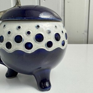 May include: A ceramic jar with a lid, featuring a navy blue and white design. The jar has a rounded shape with three small feet and a lid with a silver handle. The white section is decorated with navy blue circles.