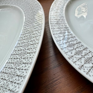 May include: Two white oval ceramic plates with a brown geometric pattern around the edge.