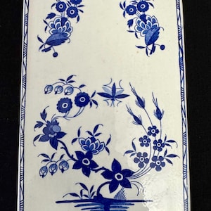 Könnte beinhalten: Eine weiße Keramikfliese mit einem blauen und weißen Blumendesign. Die Fliese hat einen gewellten Rand und einen Rand aus blauen und weißen Linien.