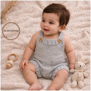 May include: A baby wearing a light gray knitted romper with wooden buttons and a front pocket. A wooden teething ring and a stuffed bunny are nearby. The text "BEE ROSE BOUTIQUE" is in a circular logo.