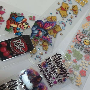 May include: Assortment of colorful stickers featuring cartoon characters, including Winnie the Pooh, Tigger, and a butterfly.  Other stickers include a can of Dr Pepper, a heart with the text "Always Believe in the Impossible", and a floral design with the text "Let it Hurt, Let it Heal".