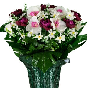 May include: A bouquet of white and pink orchids and small white flowers in a green pot. The flowers are arranged in a vase with green leaves.
