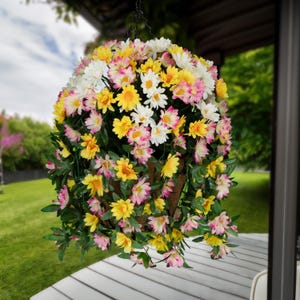 May include: A hanging flower basket filled with pink, white, and yellow artificial daisies. The basket is made of woven material and has a rustic look.