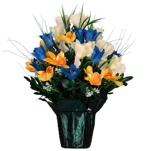 May include: A vibrant floral arrangement featuring a mix of artificial flowers in a dark green pot. The bouquet includes blue, orange, and white flowers with green foliage and long, thin stems. The pot has a shiny, textured appearance.