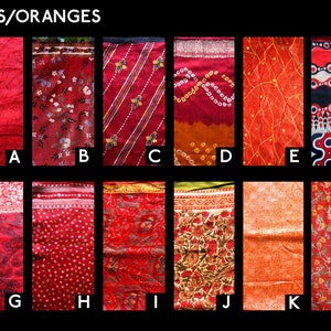 Op de afbeelding: Een collectie van twaalf stoffenstalen gelabeld A tot en met L onder de kop REDS/ORANGES. Elke staal toont een uniek patroon in rood- en oranjetinten, waaronder bloemmotieven, geometrische vormen, strepen en tie-dye ontwerpen op textiel.