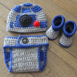 May include: A crocheted baby outfit in gray and blue with a R2-D2 design. The outfit includes a hat, diaper cover, and booties.