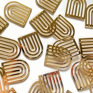 May include: A collection of gold-colored metal arch shapes with a geometric design. The arches are arranged in a random pattern on a white background.