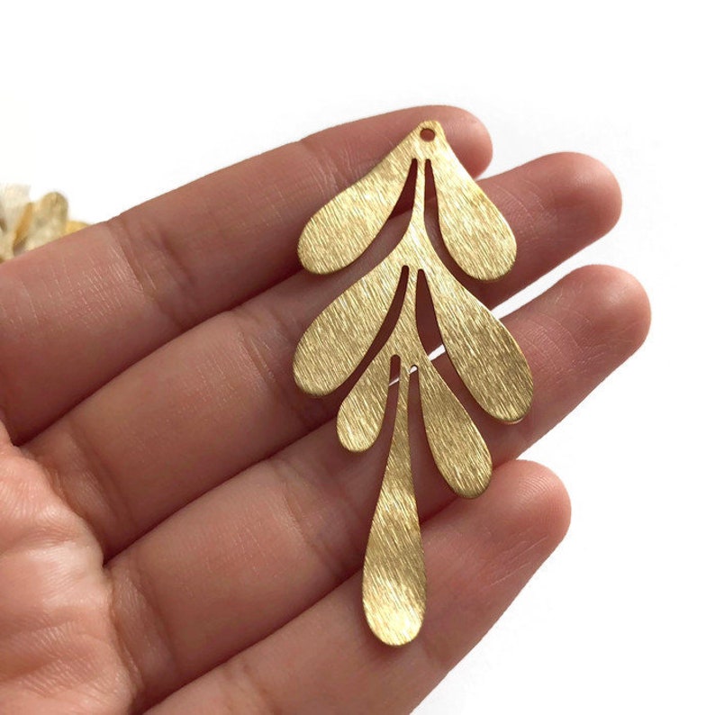 May include: Gold metal leaf charm with a brushed finish and a delicate, intricate design. The charm is shaped like a branch with multiple leaves.