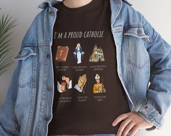 May include: A brown t-shirt with the text "I'M A PROUD CATHOLIC" and illustrations of religious symbols, including a bible, a praying hand, a church, and a pope.