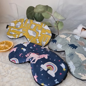 Könnte beinhalten: Drei Schlafmasken mit verschiedenen Mustern. Eine ist gelb mit einem Giraffenmuster, eine ist blau mit einem Einhorn- und Regenbogenmuster und eine ist grün mit einem Dinosauriermuster.