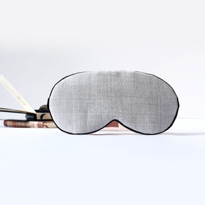 Peut inclure: Un masque de sommeil gris avec une bordure noire. Le masque est fait d'un tissu doux et texturé.