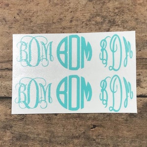 Pode incluir: Quatro adesivos de monograma azul turquesa, dois com um design circular e dois com um design de escrita. Os adesivos estão em um fundo branco.