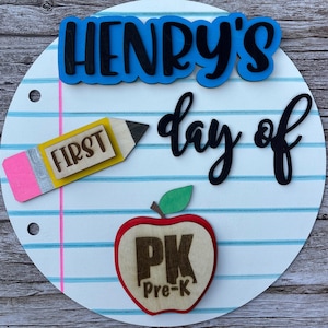 May include: A circular sign designed to look like a piece of lined notebook paper with a pink margin line. It features the blue text "HENRY'S", the black text "day of", a yellow pencil cutout labeled "FIRST", and a red apple labeled "PK Pre-K".