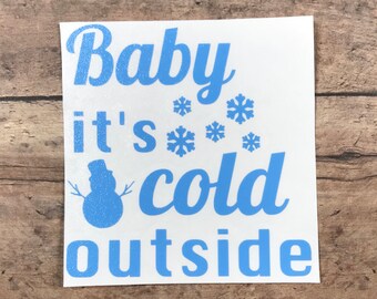 以下が含まれることがあります： 「Baby it's cold outside」というテキストと雪だるまのグラフィックが描かれた青いビニールステッカーです。