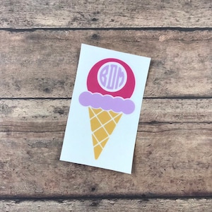 Op de afbeelding: Een sticker in de vorm van een roze, paarse en gele ijshoorn met het monogram "BDM" in een cirkel op de bovenste bol.