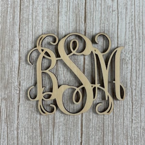 May include: A light-colored wooden monogram cutout featuring the letters B, S, and M in an interlocking script font. The design displays decorative swirls and flourishes throughout the interconnected characters, creating a continuous, ornate, and balanced shape.