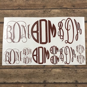 May include: A sheet of white vinyl with multiple brown monogram decals. The monograms are in a variety of styles, including a traditional script and a circular design. The decals are perfect for adding a personalized touch to any project.