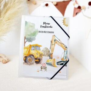 Könnte beinhalten: Ein weißer Ordner mit einer Aquarellillustration von Baumaschinen, darunter ein gelber Muldenkipper und ein Bagger. Der Text "Meine Kunstwerke ANTON MUSTERMANN" ist auf dem Cover abgedruckt, zusammen mit einer Sonne und einem Baum.