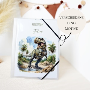 Könnte beinhalten: Eine transparente Kunststoffmappe mit einer Aquarellillustration eines Tyrannosaurus Rex. Die Mappe trägt den Text "KUNSTMAPPE Julius" und eine runde Grafik mit der Aufschrift "VERSCHIEDENE DINO MOTIVE". Ein schwarzes Gummiband sichert die Mappe.