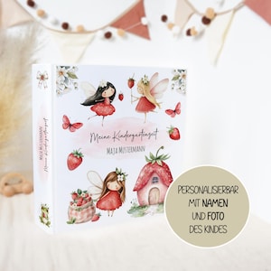 Könnte beinhalten: Ein weißer Ordner mit Aquarellillustrationen von Feen, Erdbeeren und einem erdbeerförmigen Haus. Der Text lautet Meine Kindergartenzeit und Maja Mustermann. Der Buchrücken zeigt ebenfalls den Text Maja Mustermann und Meine Kindergartenzeit.