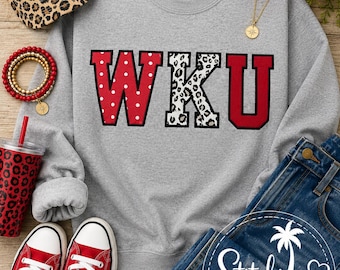May include: A heather grey crewneck sweatshirt featuring the letters WKU in a collegiate font. The W is red with white polka dots, the K is white with a black leopard print, and the U is solid red with a black outline. The fabric is a cotton blend.