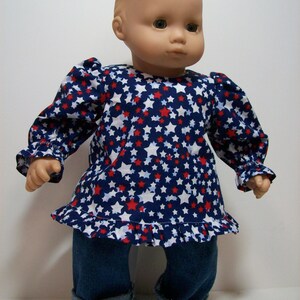 May include: A doll wearing a blue, red, and white star-patterned shirt with a ruffled hem and blue denim jeans.
