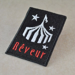 May include: Black embroidered patch with a white tent and stars, and the word "Rêveur" in red.