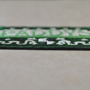 May include: Green embroidered patch with white lettering that reads "Paddy's". The patch has a decorative border.