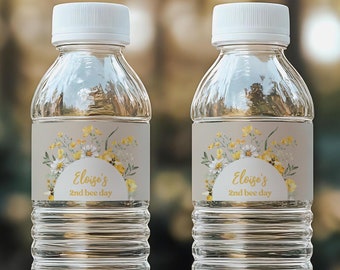 Op de afbeelding: Twee doorzichtige plastic waterflessen met gele en witte bloemenlabels waarop "Eloise's 2nd bee day" staat.