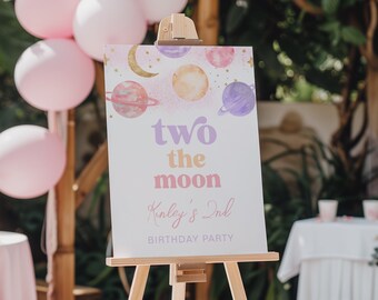 May include: A white sign with a watercolor design of planets and stars. The sign reads "two the moon Kinley's 2nd Birthday Party". The sign is on a wooden easel.