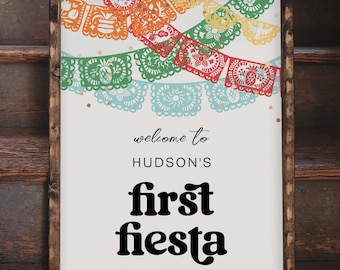 Puede incluir: Un letrero rectangular en un marco de madera teñida oscura con fondo blanco e ilustraciones de banderas de papel picado en naranja, amarillo, verde, rojo y azul. El texto dice: welcome to HUDSON'S first fiesta en color negro.