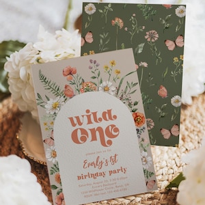 May include: A beige invitation card with a floral border and the text "wild one" in orange, featuring "Everly's 1st birthday party" details. Behind it, a dark green card displays a repeating pattern of small flowers and butterflies.
