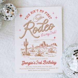 May include: A cream-coloured birthday invitation with a rodeo theme. The design features a cowboy hat, rope, and desert landscape illustration. Text reads "This ain't my first Rodeo it's my 2nd!" and "Georgia's 2nd Birthday".