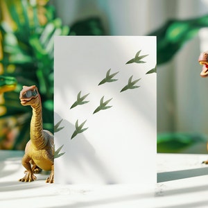 Może przedstawiać: Biała kartka z zielonym wzorem odcisk&oacute;w st&oacute;p dinozaura. W pierwszym planie znajduje się ż&oacute;łta zabawka dinozaura.