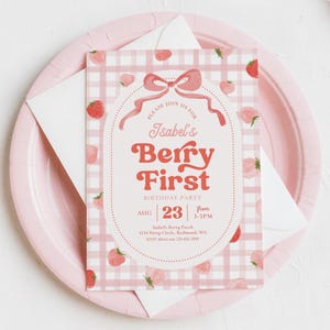 Peut inclure: Une invitation rose et blanche pour la f&ecirc;te d'anniversaire Berry First d'Isabel. L'invitation pr&eacute;sente un motif vichy rose avec des illustrations de fraises. Le texte comprend la date, l'heure et le lieu.