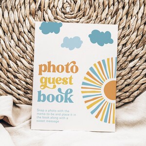 K&ouml;nnte beinhalten: Eine wei&szlig;e Karte mit einem Retro-Design mit einer Sonne, Wolken und dem Text "photo guest book". Der Text unter dem Titel lautet "Machen Sie ein Foto mit der werdenden Mutter und legen Sie es zusammen mit einer s&uuml;&szlig;en Nachricht in das Buch."