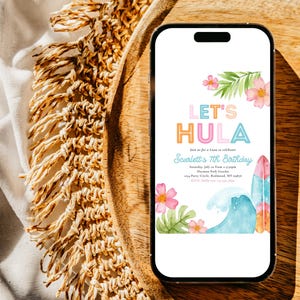 May include: A smartphone displays a colorful invitation with the text "Let's Hula" for Scarlett's 7th birthday. The design includes pink flowers, green leaves, a wave, and a surfboard. The phone rests on a wooden tray.