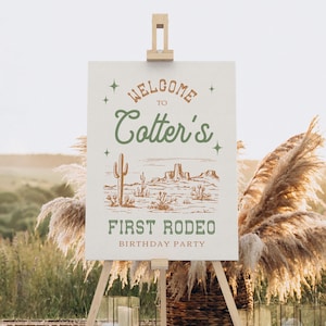 K&ouml;nnte beinhalten: Ein wei&szlig;es Schild mit braunem und gr&uuml;nem Text, auf dem "Willkommen zu Cotter's First Rodeo Birthday Party" steht. Das Schild zeigt eine Zeichnung einer W&uuml;stenlandschaft mit Kakteen und Bergen.
