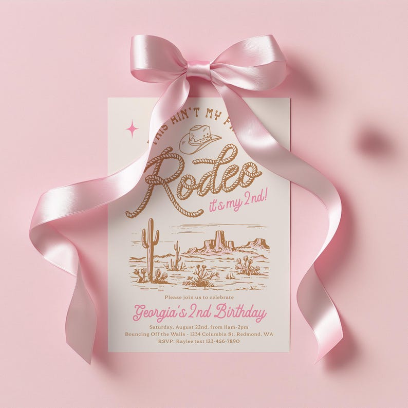 May include: A rectangular invitation card with a pink satin bow at the top. The card features a brown western-themed illustration of a cowboy hat, rope-style text reading "This ain't my first rodeo, it's my 2nd!", and a desert landscape with cacti.