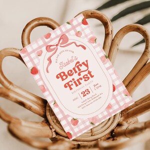 Peut inclure: Une invitation d'anniversaire rose et blanche &agrave; carreaux vichy avec le texte "Isabel's Berry First". L'invitation pr&eacute;sente un th&egrave;me de fraises avec des illustrations de fraises et un n&oelig;ud d&eacute;coratif. La date est le 23 ao&ucirc;t.