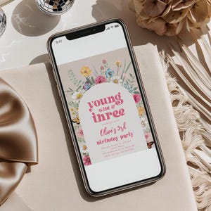 May include: A digital invitation for a birthday party with a floral archway design. The text reads "young wild & three" and "Olive's 3rd birthday party".