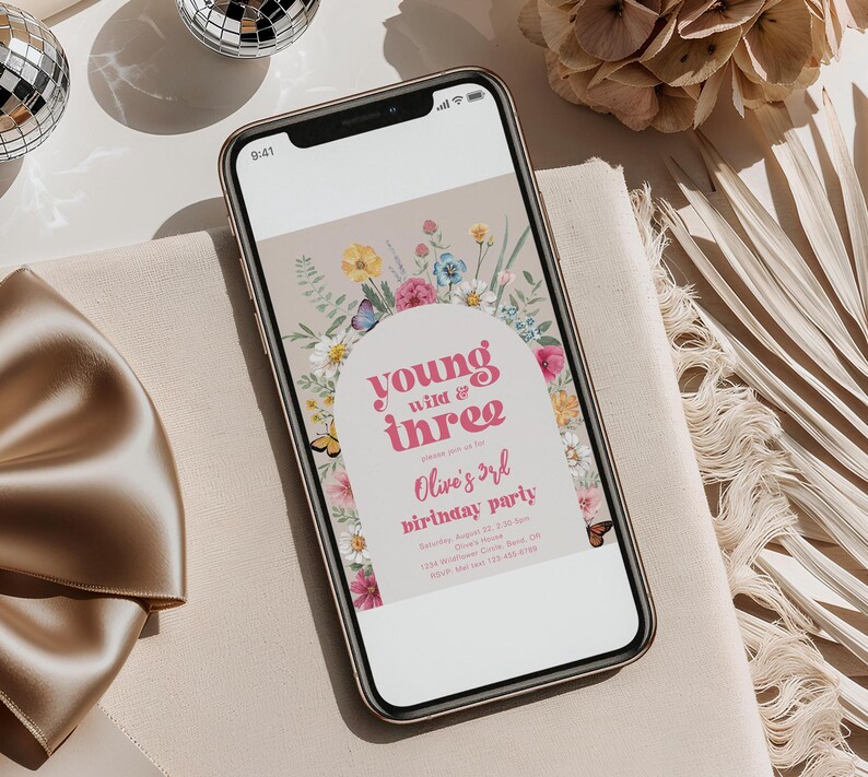 May include: A digital invitation for a birthday party with a floral archway design. The text reads "young wild & three" and "Olive's 3rd birthday party".
