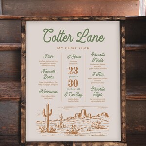 K&ouml;nnte beinhalten: Ein beige-braunes illustriertes Poster mit dem Text "Cotter Lane Mein erstes Jahr". Das Poster listet die Lieblingsdinge eines Kindes auf, darunter B&uuml;cher, Lebensmittel, Spielzeug und Aktivit&auml;ten. Das Poster ist mit einer W&uuml;stenlandschaft-Illustration verziert.