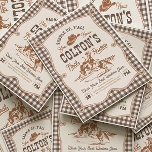 Op de afbeelding: Een stapel rechthoekige uitnodigingen met een bruin-witte vichy-ruitrand. De centrale tekst luidt "Saddle up, y'all", "Colton's First Rodeo" en "Wear Your Best Western Gear", vergezeld van illustraties van een cowboyhoed en een bokkend paard.