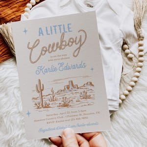 Op de afbeelding: Een lichtbruine uitnodiging met een blauw en bruin touwontwerp met de tekst "A Little Cowboy" en een illustratie van een westelijk landschap. De uitnodiging is voor een babyshower voor Karlie Edwards. De tekst luidt: "Zaterdag 22 april, van 15:00 tot 18:00 uur, Houston Country Club, 1 Potomac St. Houston, TX, RSVP: Kaylee text 123-456-7890, Geregistreerd bij babulist.com/karlie-edwards"